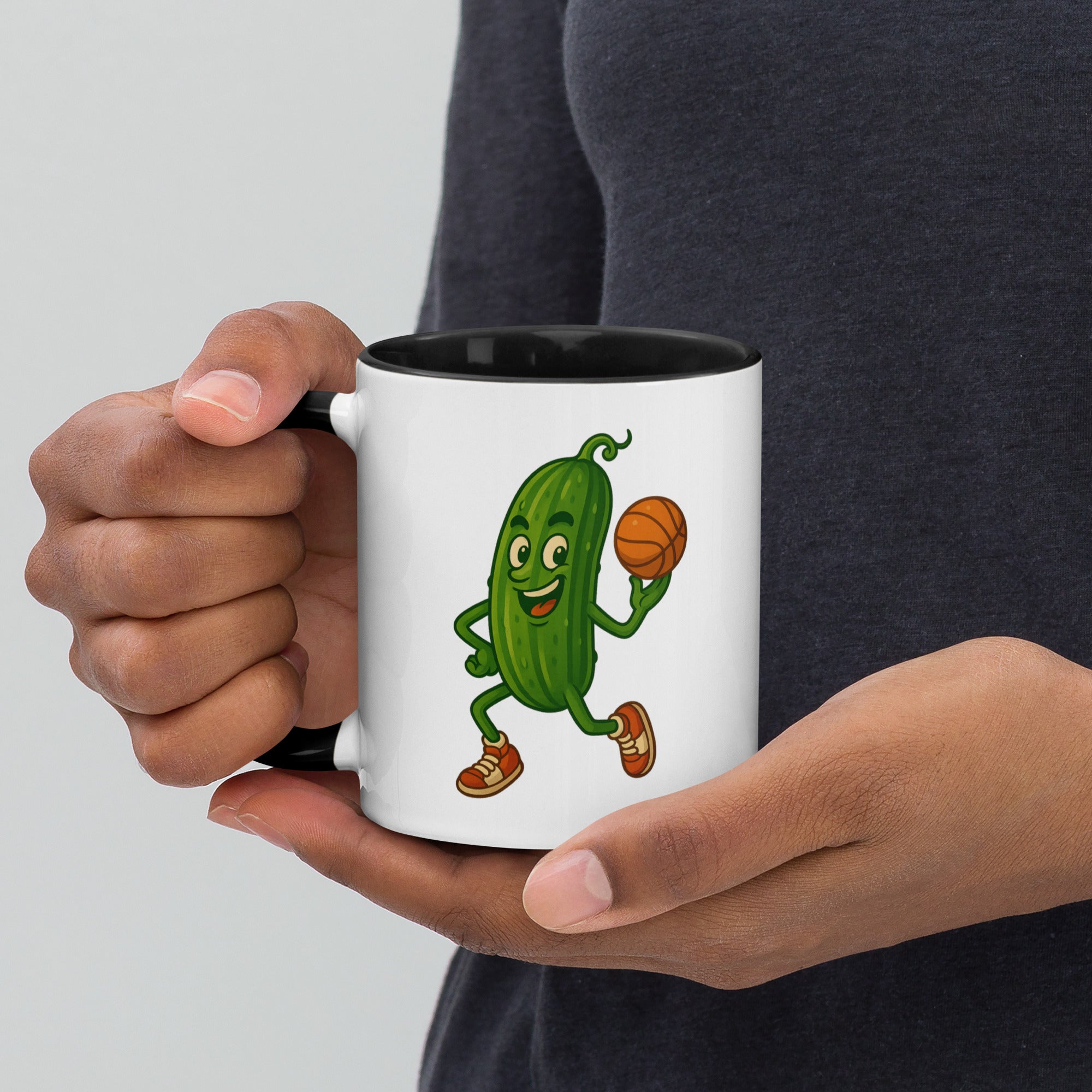 Person holding a whimsical pickle-themed ceramic mug with black interior and basketball design.