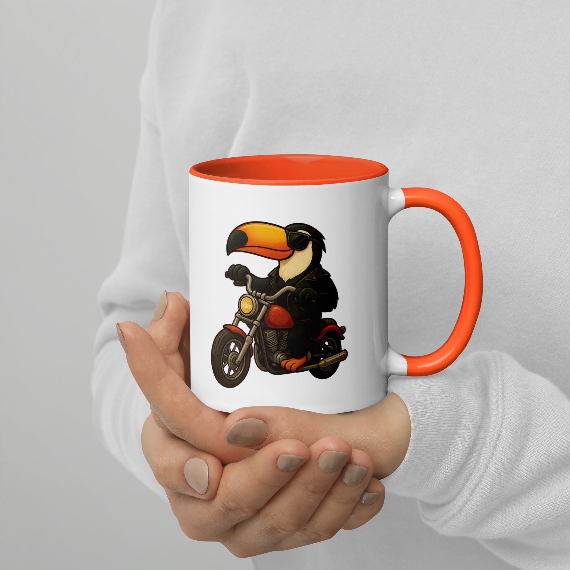 Mug with toucan on a motorcycle design held by a person against a light gray background